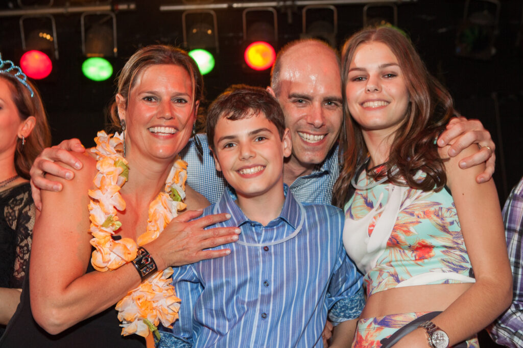 Four people smiling and posing closely together at an indoor event, with colorful lights visible in the background.