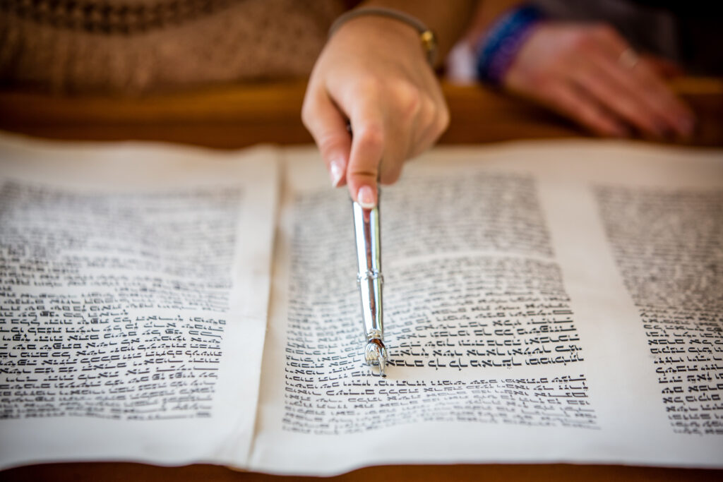 A person uses a silver pointer to read text written in Hebrew on a Torah scroll.