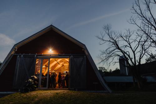 Western MA Wedding Photographer captures a stunning image of a red barn at dusk, with two people elegantly posed in front of it.