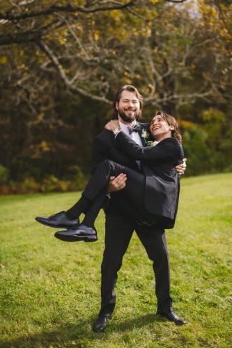 In this breathtaking wedding photography moment, a bride carries her groom, both beautifully dressed in tuxedos. This stunning image captures the essence of love and celebration, making it a top contender