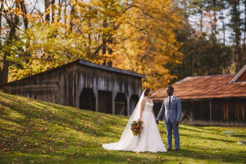 A Western MA Wedding Photographer captures a bride and groom standing in front of a barn in the fall.