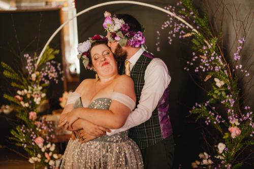 A bride and groom hugging in front of a floral arch captured by a Western MA Wedding Photographer.
