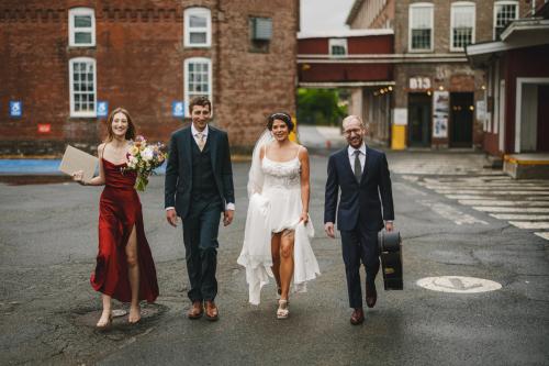 A group of bridesmaids and groomsmen walking in front of a brick building captured by a Western MA Wedding Photographer.
