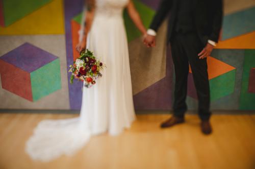 A Western MA Wedding Photographer captures a beautiful moment of a bride and groom holding hands in front of a colorful wall.