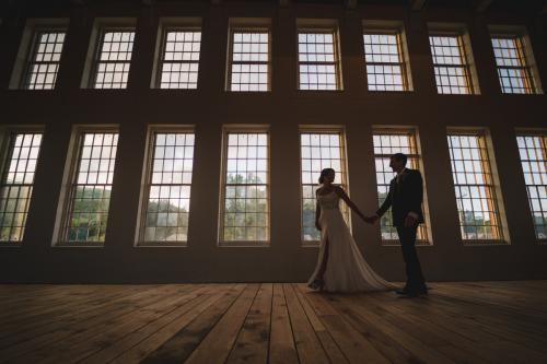 A Western MA Wedding Photographer captures a bride and groom standing in front of large windows.