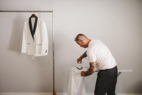 A Western MA Wedding Photographer captures images of a man donning a white suit on a hanger.