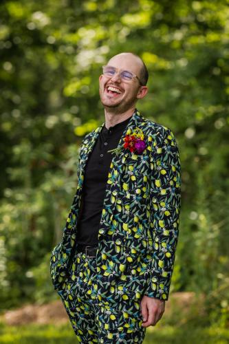 A Western MA Wedding Photographer captures a man in a colorful suit smiling in the woods.