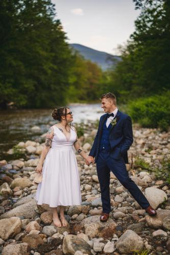 A Western MA Wedding Photographer captures a bride and groom standing on rocks near a river.