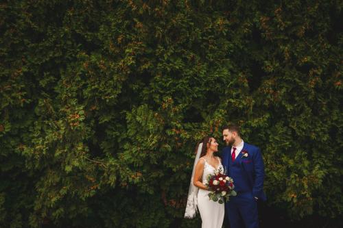 A Western MA Wedding Photographer captures a bride and groom standing in front of a hedge.
