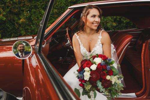 A Western MA Wedding Photographer captures an enchanting bride sitting elegantly in the back seat of a classic car, clutching her beautiful bouquet.