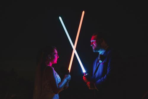 A Western MA Wedding Photographer captures a bride and groom wielding light sabers at night.