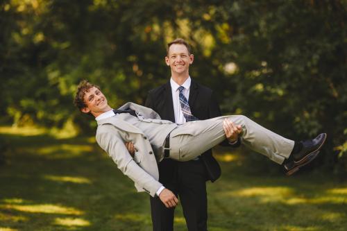 A Western MA Wedding Photographer captures a stunning moment of a man in a suit being carried by another man in a suit.
