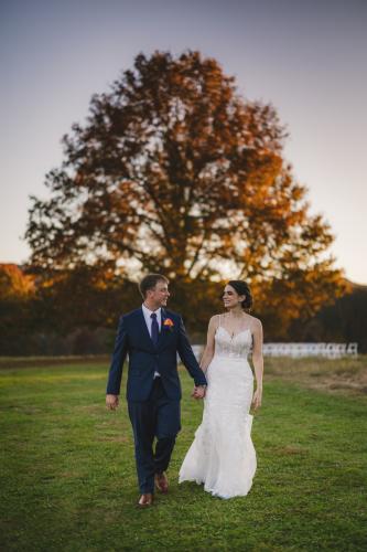 A Western MA Wedding Photographer captures a bride and groom walking through a field at sunset.
