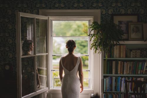A Western MA Wedding Photographer captures a stunning image of a bride in a wedding dress looking out of an open window.