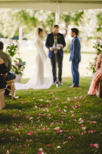 A beautiful wedding ceremony under a tent in Western MA, captured by a talented wedding photographer. The picturesque setting features vibrant flowers scattered on the ground, adding to the romantic atmosphere.