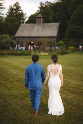 As a Western MA Wedding Photographer, I capture beautiful moments like a bride and groom walking through a grassy field with a barn in the background.