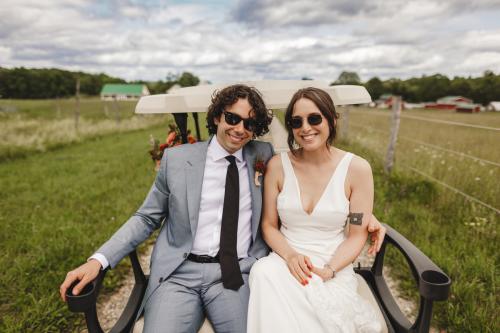 A Western MA Wedding Photographer captures a bride and groom sitting on a golf cart in a field.