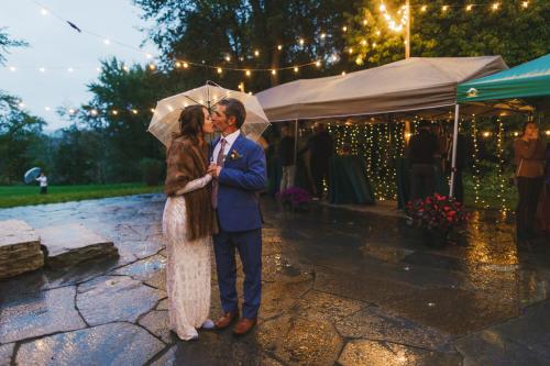 A bride and groom share a romantic kiss under a string of lights, captured beautifully by a Western MA wedding photographer.