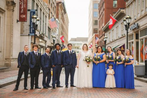 A group of bridesmaids and groomsmen pose for a photo on a cobblestone street, captured beautifully by a Western MA Wedding Photographer.